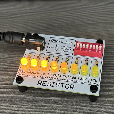 Hands On Soldering Practice Kit resistor board with LED lights, Ohm's Law diagram, and DIP switch on gray surface