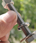 Close-up of a Tough-As-Nails 3/8-16 X 5 stainless steel hex bolt with nut and washers in hand, fully threaded, outdoor backdrop.