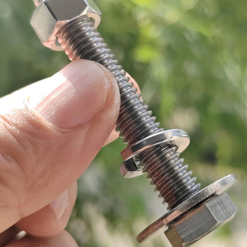 Close-up of a Tough-As-Nails 3/8-16 X 5 stainless steel hex bolt with nut and washers in hand, fully threaded, outdoor backdrop.