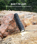 M70 EDC Flashlight 1100 Lumens USB C Rechargeable Pocket Light with Clip on wet rocks, durable for outdoor use.