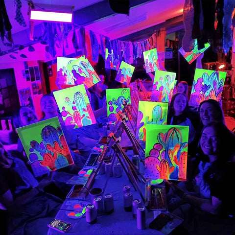 Art studio with people painting glowing posters under Two Pack 100W LED Black Light Bar 385-400nm Ultra Bright UV Glow Lights