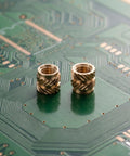 Premium 48Pcs Brass M4 Heat Set Threaded Inserts For 3D Printing placed on a green circuit board showcasing their knurled design.