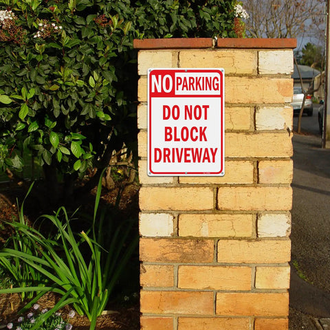 Heavy Duty No Parking And Do Not Block Driveway Sign 14X10 Inch Reflective Aluminum mounted on a brick post in a garden.