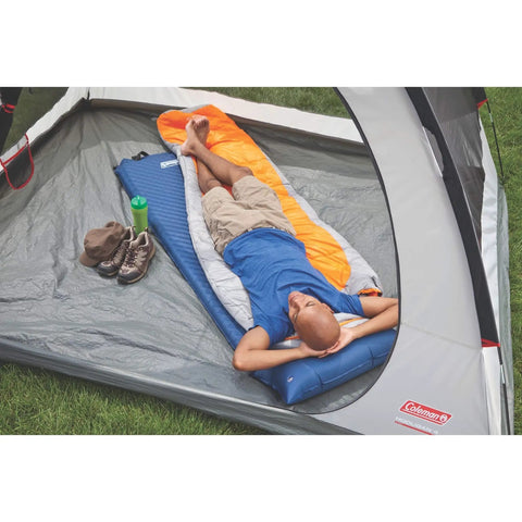 Person relaxing on self-inflating sleeping pad with pillow in a tent, showcasing cushioned comfort for comfy nights while camping.