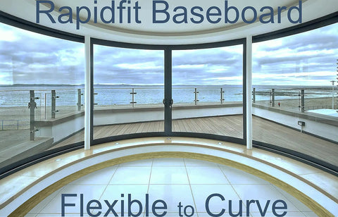 Curved glass window with vinyl baseboard, showing flexibility. Moisture Resistant Vinyl Baseboard Molding With Wood Grain Finish Quarter Inch Thick Four Inch Tall Rubber Wall Base Trim Waterproof Base Molding For Bathrooms Basements Garages Sixteen Foot Length Easy Install.