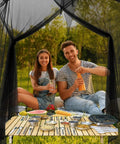 Two people dining inside a 10x10x8.2 Ft Outdoor Mosquito Netting For Camping Patio And Travel with black mesh and hanging ropes.