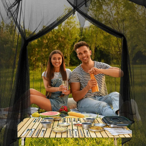 Two people dining inside a 10x10x8.2 Ft Outdoor Mosquito Netting For Camping Patio And Travel with black mesh and hanging ropes.