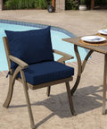 Outdoor Dining Chair Cushion Set 21 By 21 Inches In Sapphire Blue Rainproof And Fade Resistant Includes One Back Pillow And One Seat Bottom Eco Friendly PFAS Free C0 Treatment With Recycled Polyfill And Polyester Fill Fits Most Chairs on a wooden chair by a poolside table.