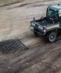 Rugged 6 Foot By 4 Foot Tow Behind Drag Harrow With Powder Coat Black Finish attached to ATV on soil field, 97 tines visible