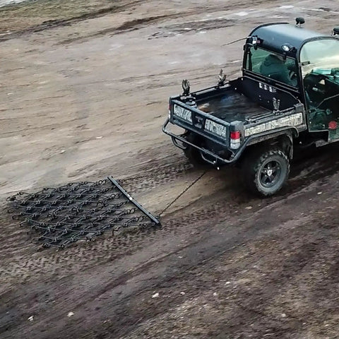 Rugged 6 Foot By 4 Foot Tow Behind Drag Harrow With Powder Coat Black Finish attached to ATV on soil field, 97 tines visible