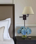 Set Of 2 Modern Swing Arm Wall Sconces With Latte Mocha Empire Fabric Shade next to bed with blue flowers on nightstand