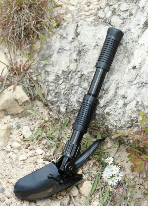 Compact Folding Shovel With Pick For Camping and Backpacking Lightweight Essential Tool leaning against rock outdoors