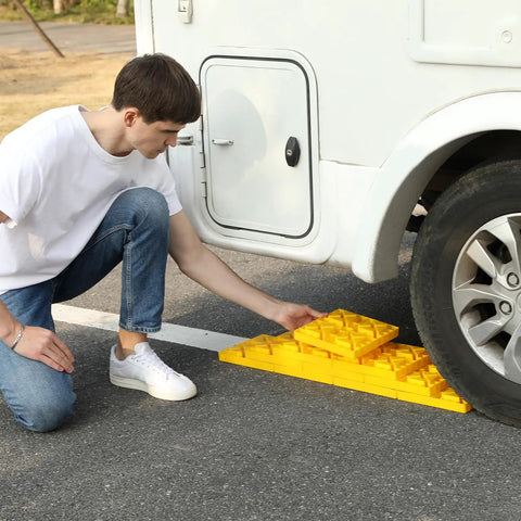 Person installing Ten Pack RV Camper Leveling Blocks With Interlocking Design Non Slip Pads under a travel trailer wheel.