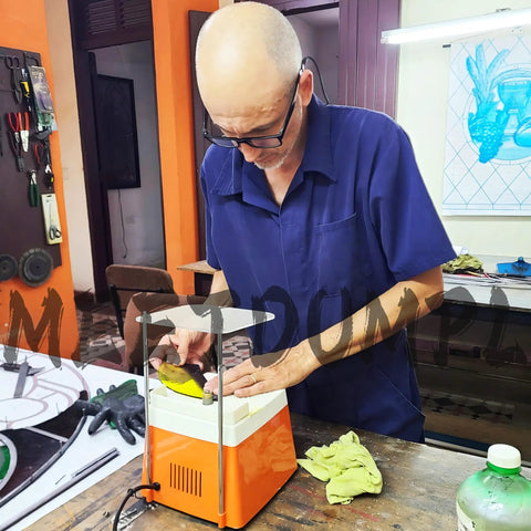 Adult using orange glass grinder in workshop with stained glass tools and materials.