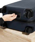 Close-up of navy Bigger Carry On Luggage From Away, featuring spinner wheels and TSA lock, on a stone surface.