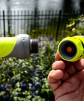 Connecting quick-connect adapter to green garden hose nozzle in a garden setting, part of Garden Hose Nozzle Kit, 3-Piece With Quick Connect Sprayer And Flow Stop Adapter.