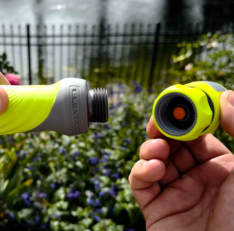 Connecting quick-connect adapter to green garden hose nozzle in a garden setting, part of Garden Hose Nozzle Kit, 3-Piece With Quick Connect Sprayer And Flow Stop Adapter.