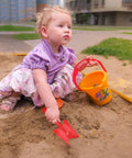 Child playing in sandbox with a red hand shovel from the 20 Pack Mini Colorful Metal Hand Shovels And Trowels Set For Transplanting And Garden Digging.