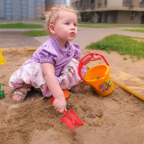 Child playing in sandbox with a red hand shovel from the 20 Pack Mini Colorful Metal Hand Shovels And Trowels Set For Transplanting And Garden Digging.