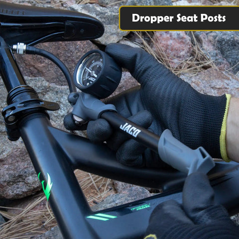 Cyclist using ShockPro MTB Shock Pump With 300 PSI High Pressure Gauge on mountain bike dropper seat post in rocky terrain.