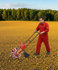 Person using Manual Garden Push Seeder With 7 Nozzles And Eight Pound Seed Box Easy To Use Depth Settings One To Three Inches Red