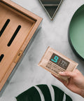 Hand holding 72% RH pack next to wooden storage box, part of Starter Kit Bundle For Wooden Storage Box With Two Way Humidity Control Keeps Your Box On Point At Exact RH Levels Includes Two 60 Pack Humidity Packs At 84 Percent RH And 72 Percent RH.