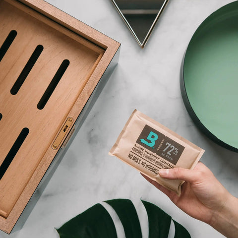 Hand holding 72% RH pack next to wooden storage box, part of Starter Kit Bundle For Wooden Storage Box With Two Way Humidity Control Keeps Your Box On Point At Exact RH Levels Includes Two 60 Pack Humidity Packs At 84 Percent RH And 72 Percent RH.