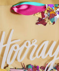 Close-up of a Medium Gift Bag With Tissue Paper And Hooray Confetti Design in gold with pink teal purple ribbon and confetti.