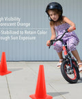 Child riding a bike between two bright orange 18 inch traffic cones built tough for weather resistance, UV-stabilized for high visibility.
