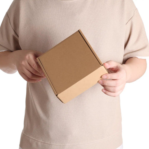 Person holding a 6x6x2 inch Rock Solid 50 Pack Small Shipping Box, brown kraft corrugated cardboard for packaging.