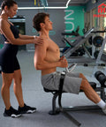 Man using Universal Belt Squat Collar For Nordic Hamstring Curl On Bench in gym, demonstrating seated exercise setup.