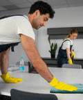 Two people cleaning a table with Premium Color Terry Cloth Rags 25 Lb Bulk Bag Super Absorbent Cotton Cleaning Rags For Garage And Shop Industrial Use And Housekeeping Multi Purpose Towels For Quick Mess Cleanups, wearing yellow gloves.