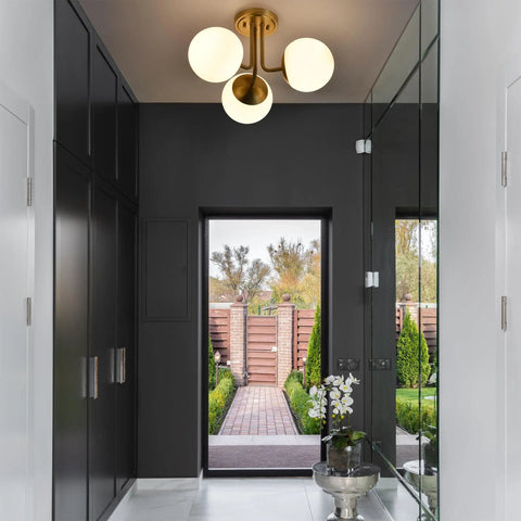 Three Light Aged Brass Semi Flush Mount Ceiling Light Fixture With White Globe Glass in modern hallway setting.