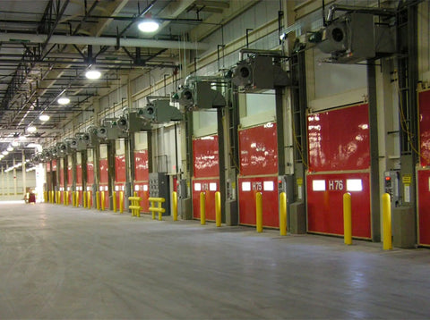 Interior view of loading bays with red doors and yellow bollard post covers for protection in a warehouse.