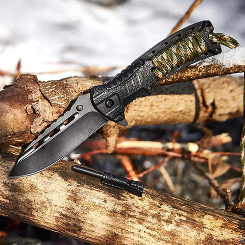 3.74 Inch Sharp Blade Folding Knife With Fire Starter Whistle Paracord Handle set on wooden logs outdoors.