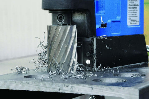 Hougen HMD904 115-Volt magnetic drill, blue and black, front view with metal shavings on a steel worktable