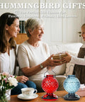 Family exchanging gifts with hummingbird feeders in front, red and blue 25 Oz Glass Hummingbird Feeder With Ant Moat And Bee Proof Feeding Ports.