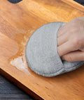 Hand using Heavy Duty Five Inch Microfiber Wood Conditioner Applicator Pad on a wooden cutting board to spread oil.