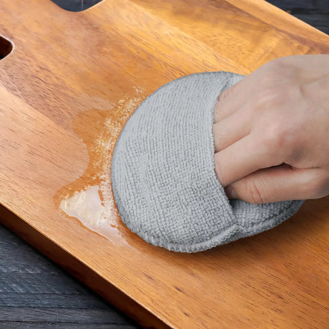 Hand using Heavy Duty Five Inch Microfiber Wood Conditioner Applicator Pad on a wooden cutting board to spread oil.