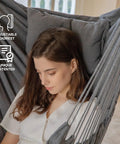 Woman sitting in dark gray hammock chair with adjustable headrest indoors, part of Hammock Chair With Stand For Indoor And Outdoor Use