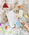 Phone case with floral design and a hand holding a credit card on a fluffy surface surrounded by colorful nuggets.