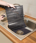 Person adjusting 2 Pack Kitchen Sink Mat Set For Stainless Steel And Ceramic Sinks, Eco Friendly PVC Bottom Protector, Black 11.8x15.7 inches.