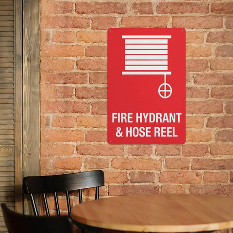 Outdoor Emergency Fire Hydrant And Hose Reel Safety Sign 8x12 Inch Wall Plaque mounted on brick wall near table and chair.