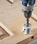 Close-up of Bosch HBT225 2-1/4 in bi-metal T-slot hole saw attached to drill cutting wood.
