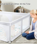 Mother watching baby in Extra Large Baby Playpen With Mat 79 By 71 Inches For Toddlers And Infants Safety Gate Play Yard In Light Gray.