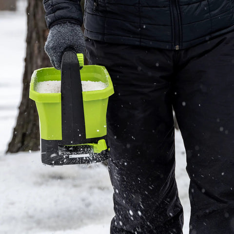Person using 20-Volt Cordless Handheld Seed And Fertilizer Spreader For Yard Work With Adjustable Spreading Rate Dial on snowy day