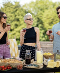 People gathered around a table with food and drinks, outdoors in a garden setting, during a casual gathering.