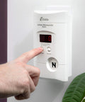 Plug-In Carbon Monoxide Detector With 9V Battery Backup, Digital LED Display, 85 Decibel Alarm on wall with finger pressing test button