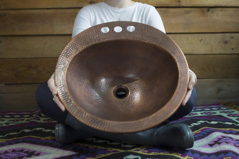 Person holding Bell Drop In Handmade Copper Bath Sink With Four Inch Faucet Holes And Overflow, showcasing antique copper texture.