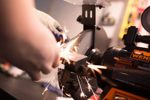 Person using the Rock Hard Bench Grinder with Eight Inch Grinding Wheels and a snappy variable speed motor, producing sparks while sharpening metal.